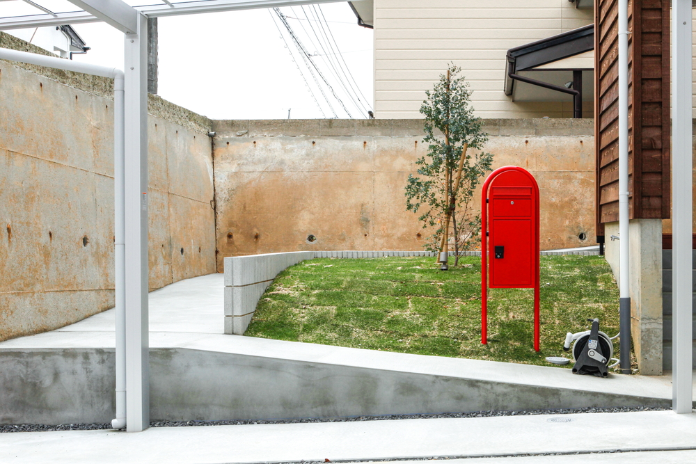 共感住宅ray-outが岡崎市でオーナーさんとつくりあげたおうちは、駐車場から玄関までスロープを設置。赤いポストと緑の芝生でカントリーな雰囲気をつくっています。