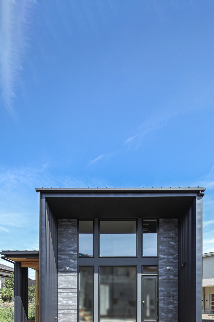 ひろいLDKを持つ家の外観は黒いガルバリウムとサイディングの壁で四角い形をしている