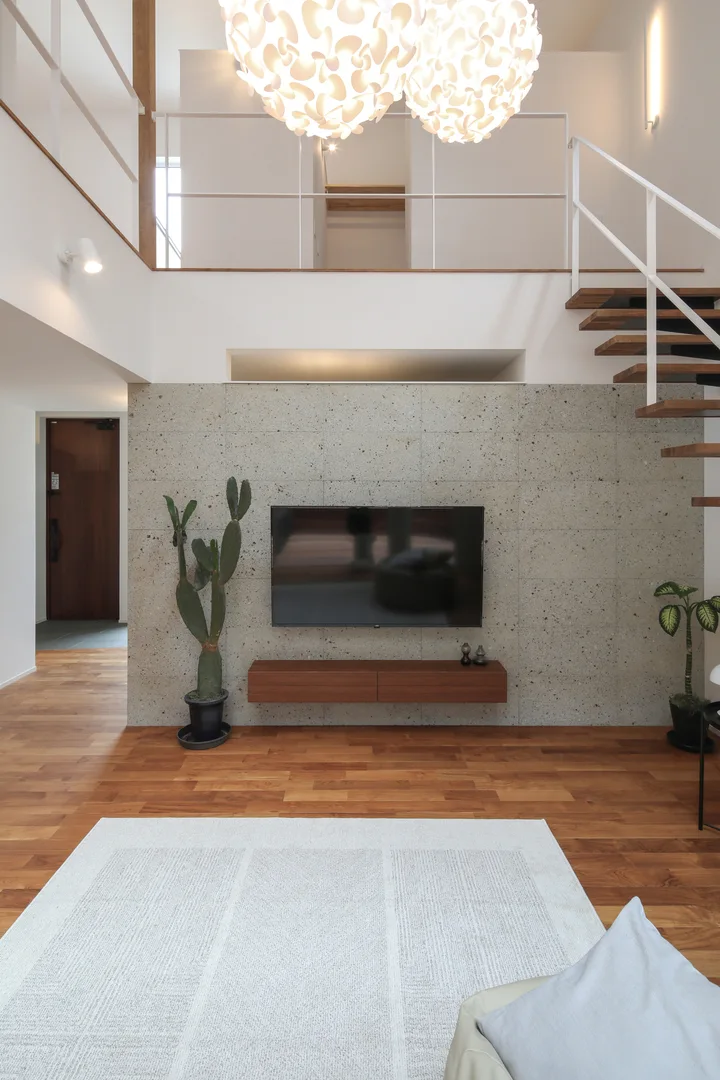 リビングにある大谷石を貼った壁と、そこにかかる壁掛けテレビ。1ｍほどの高さの観葉植物を左右に飾っている。