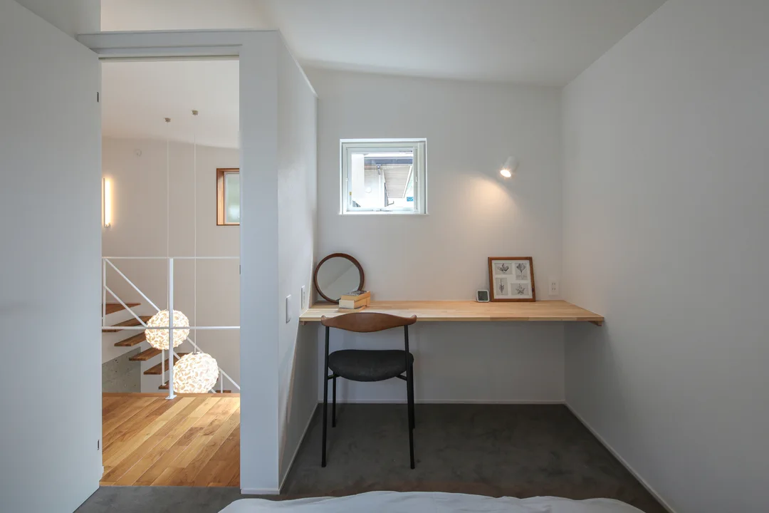 主寝室。床はグレーのタイルカーペット。1畳ほど書斎スペースがあり、備え付けのデスクがある。