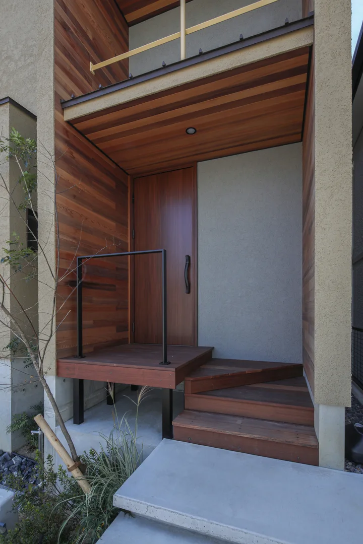 玄関ポーチ。内側に凹んでいるネガティブな空間で、壁の一部の色をグレーにしている。その他袖壁の内側と庇の天井にはレッドシダーを貼っている。転落防止に黒いアイアンバーがついていて、ポーチ部分にはウッドデッキ。