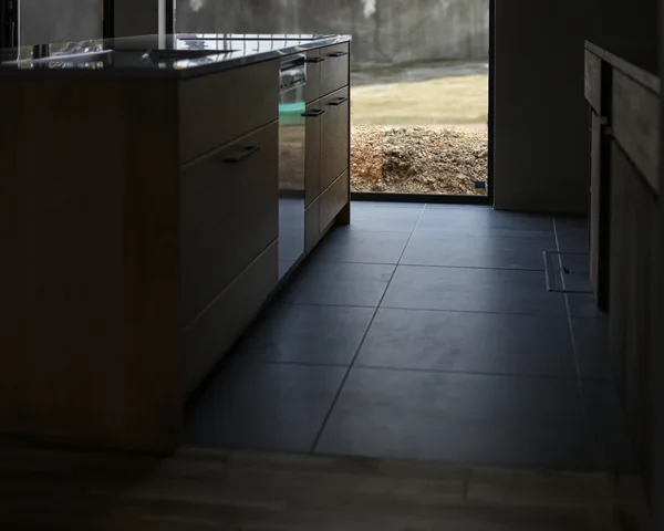 キッチンとタイルの床、手前にはアカシアの無垢フローリング、奥には窓があり外が見える