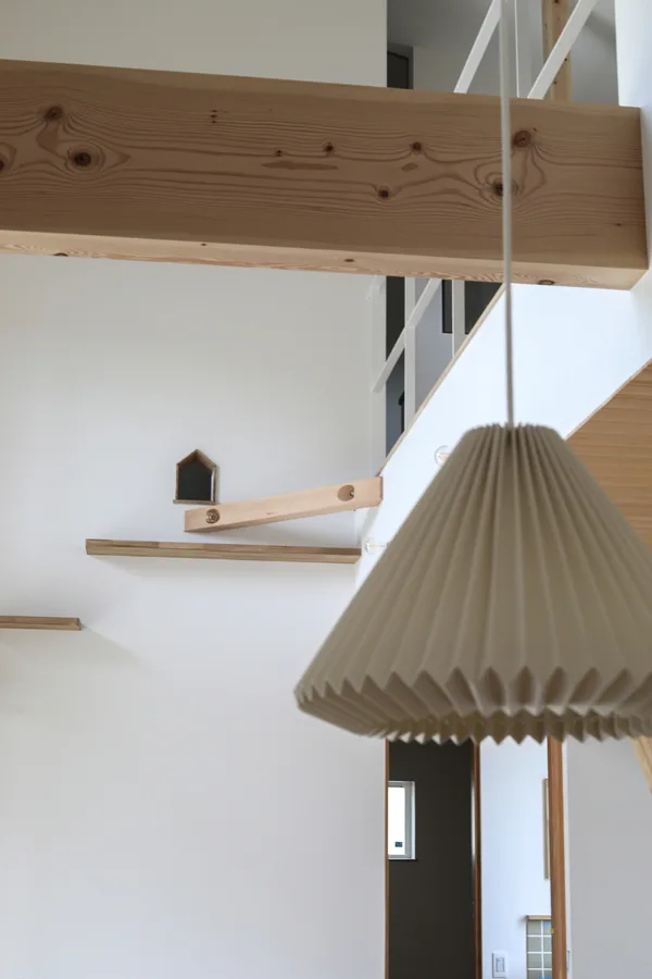 床から3ｍほどの高さに開いた壁の穴は三角屋根の家の形をしている。キャットウォーク用の板が穴の下の壁に固定されている。前景はペンダントライトのシェード