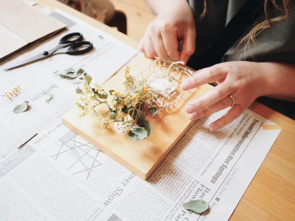 大人の片手サイズの四角い板に釘を打ち、そこに糸が掛かっている。糸はジャムの瓶のような画を描いており、ドライフラワーがその瓶に刺さっている。