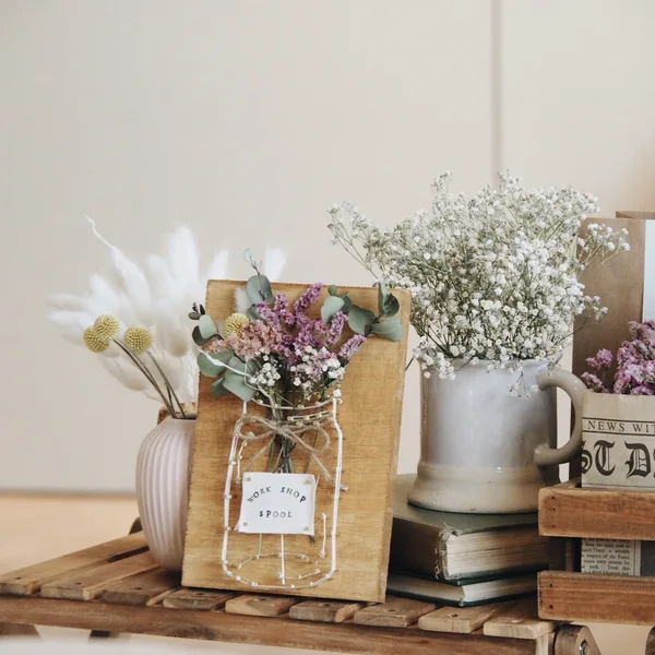 木の箱、木の板、陶器の取手付き花瓶、ドライフラワーが飾られている