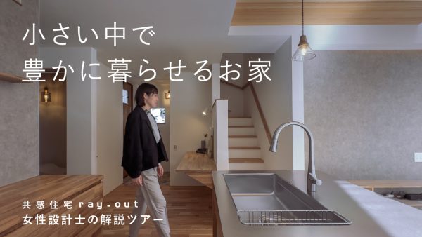 家の中を歩く女性。手前にはシステムキッチンとカップボード、奥には玄関と会談が見える。