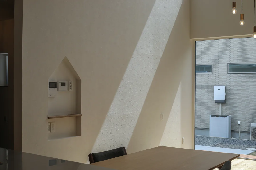 室内の壁。左側にスイッチニッチ。家形に凹んでいる。右上の吹抜け窓から光が斜めに差し込んでいる