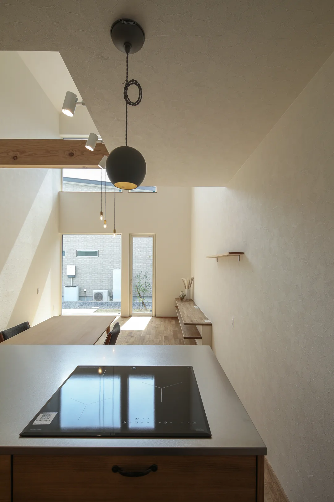 手前にキッチンのIHコンロ。真上にペンダントライト1灯。奥にリビング、庭への窓とテラスドア。
