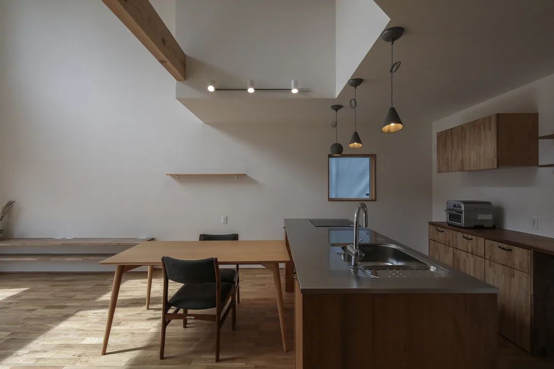 ダイニングとキッチンを真横から見た写真。キッチンはパーティータイプで天板がステンレス。キッチンの上にペンダントライト3灯。ダイニング上部は吹抜け。