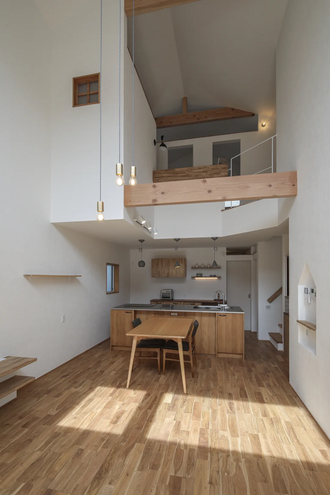 吹抜けのLDK。天井は船底天井。白いクロス。床はオークの無垢フローリング。手前からリビング、ダイニング、キッチン。ダイニングとリビングの間に太い梁が一本通っている