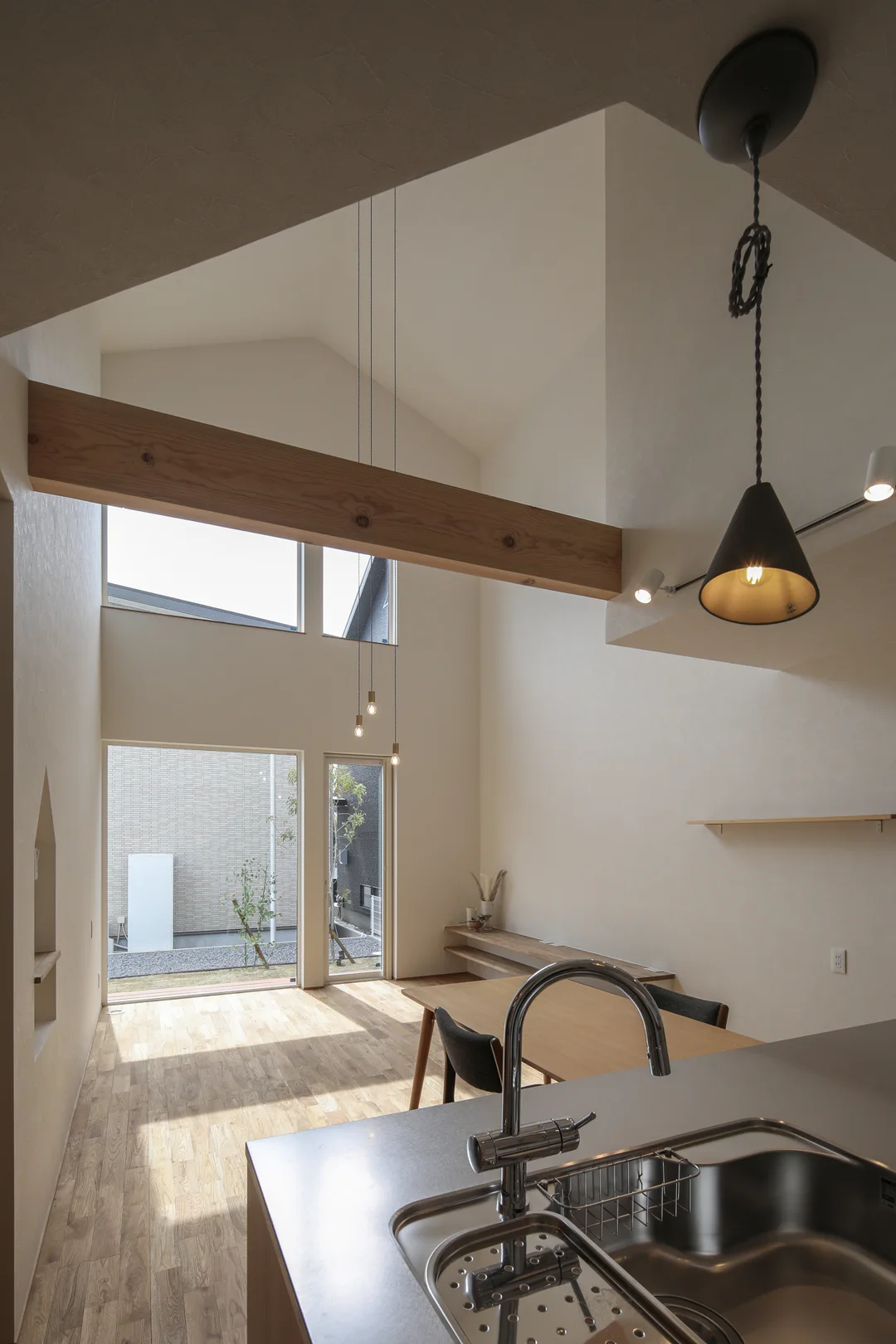 キッチンシンクから吹抜けのリビングを眺めている画。リビング天井は船底天井。窓が田の字で並んでいる。