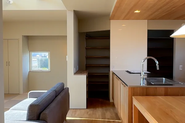 リビング。床はオークの無垢フローリング。天井に木が貼られている。奥の部屋に棚が見える