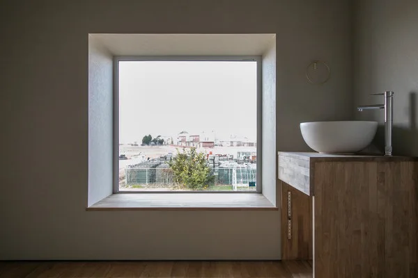 大きな四角い窓。窓はベンチになっていて、手前には洗面ボウルがある。床は無垢フローリング。