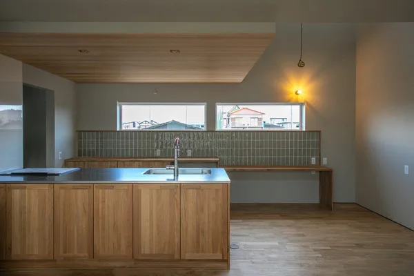 無垢の木のキッチン。背面には緑色のタイルが貼られている。天井は羽目板張りで、2つの横長の窓から外の景色が見える。