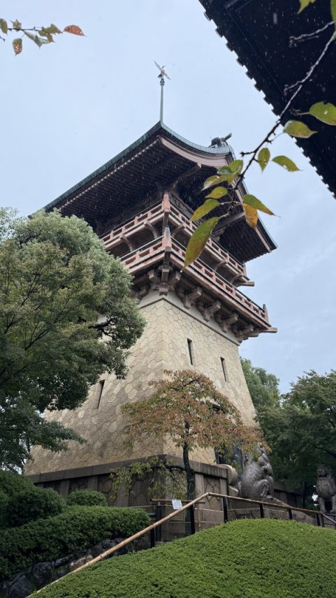 塔を下から見上げている。塔の下半分は黄色い石を積み上げた形。上には祇園祭の鉾のような建物が乗っている