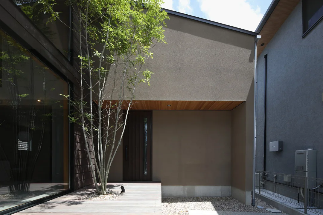 日本のモダンな住宅の外観。木が植えられた小さなデッキと、木のドアが見える。