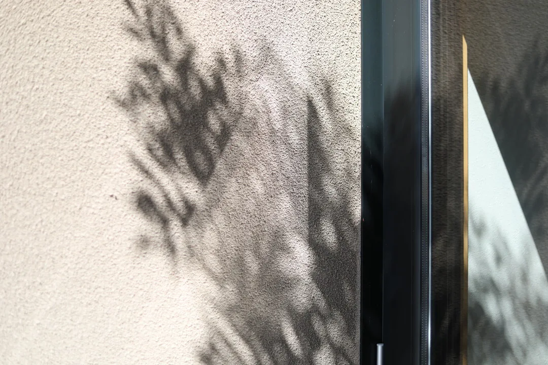 木の葉の影が壁に映っている様子。窓枠の一部が見える。壁は塗り壁。