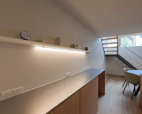 白い壁に木の葉の影が映っている。壁には薄いオレンジ色に灯るウォールライトが付いている