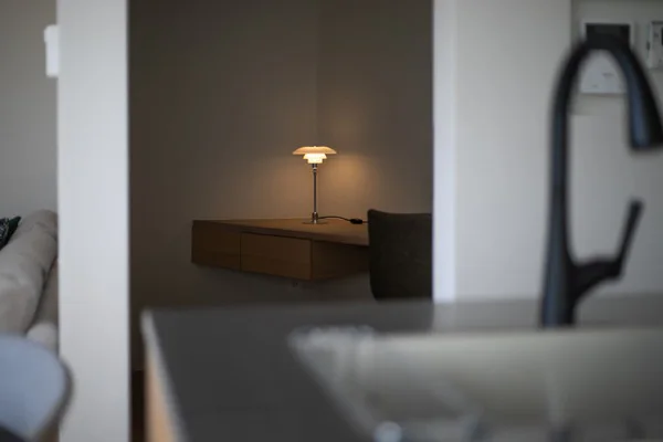 白い壁に区切られた部屋。奥に作り付けの机があり、その上にデスクライトが置かれている。
