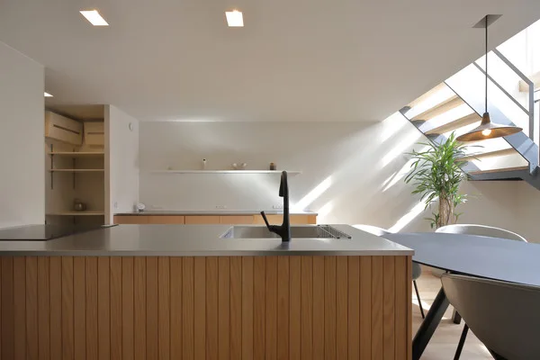 木の板が貼られたキッチン。天板はステンレス。背面には白い壁に飾り棚が付いている