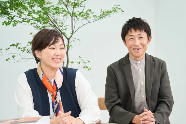 葉のついた枝を背景に、女性と男性の営業スタッフが笑顔で座っている