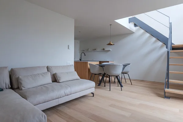 木目の床に、グレーのソファーのあるリビング。奥にはダイニングとキッチンがある。