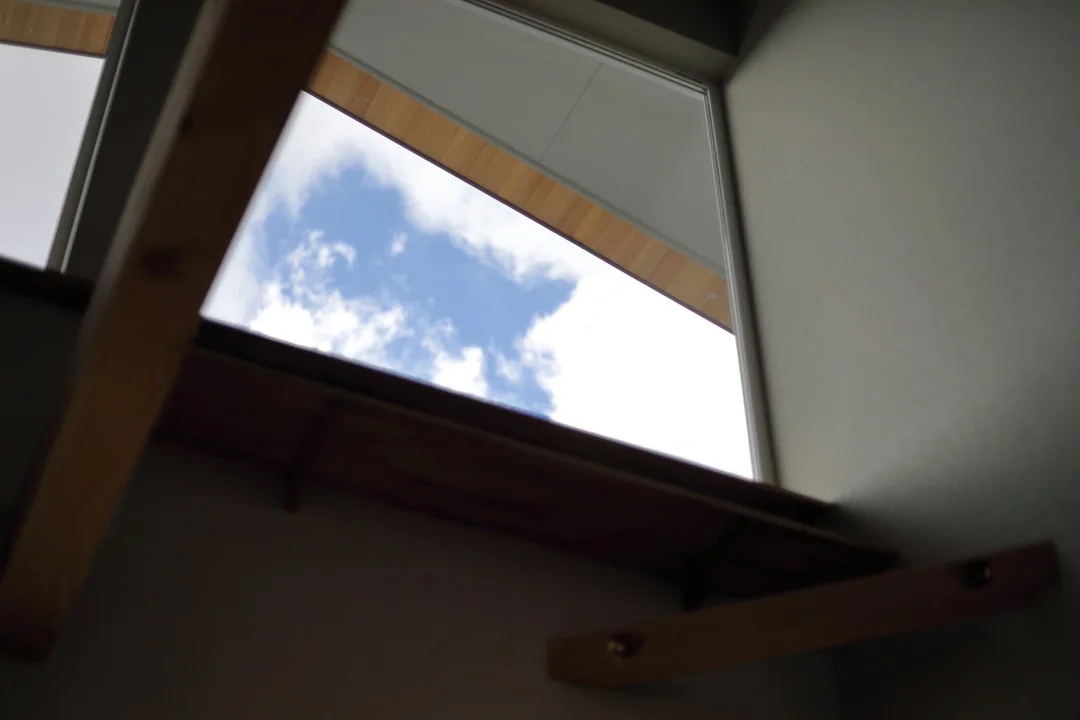 室内の吹き抜け部分から見上げた天窓。青空と白い雲が見える。