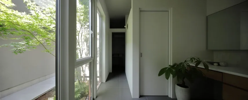 タイルの床の廊下。左手には中庭に面した大きな窓があり緑が見える。右手には造作の洗面台がある