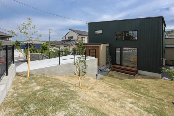 道路から大きく下がった土地に建つ家。法面には緑の芝生がある