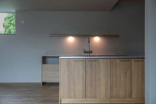 キッチン。木のキャビネット、床は無垢フローリング、壁はグレー。