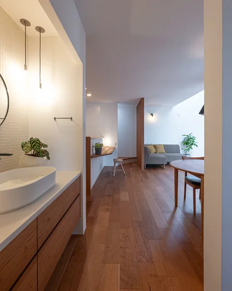 室内。アメリカンチェリーの床に、白い壁。左側には洗面があり、右手奥にはリビング置かれたソファが見える