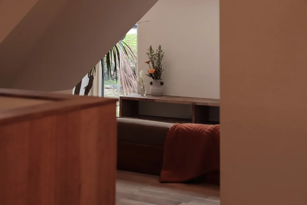 ダイニングから階段下のヌックを通してみたリビングの一角。テレビボードには花が生けられ、窓から光が入っている