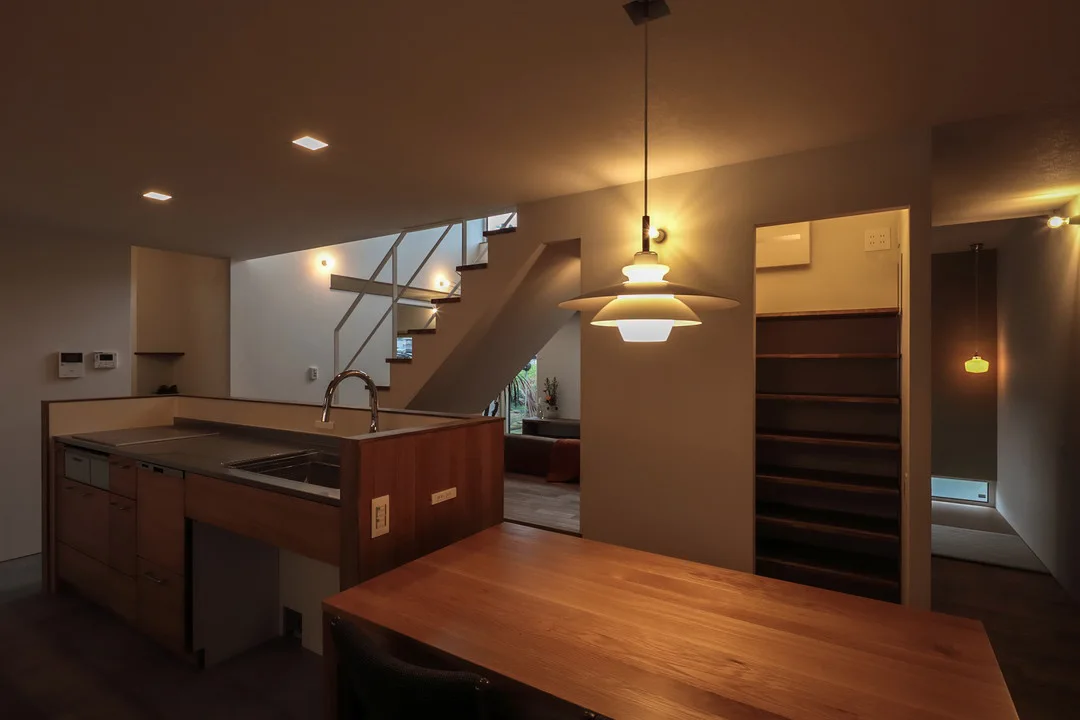 ダイニングキッチン。木製のダイニングテーブルとキッチンカウンターがあり、照明が落ち着いた空間を演出している