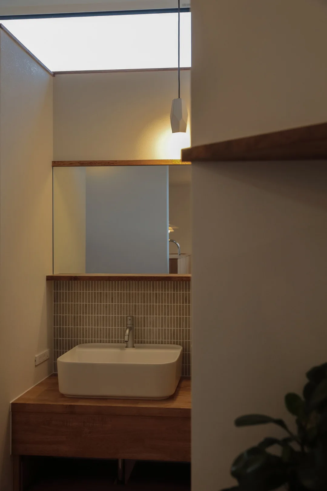 自然光が差し込む洗面台。木製カウンターに白いベッセル型ボウル、壁面にはタイルが施されている