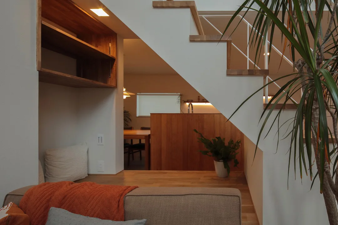 階段下のスペースを通して見たキッチンとダイニング。手前にソファ、奥に木製のキッチンカウンターがあり、落ち着いた雰囲気