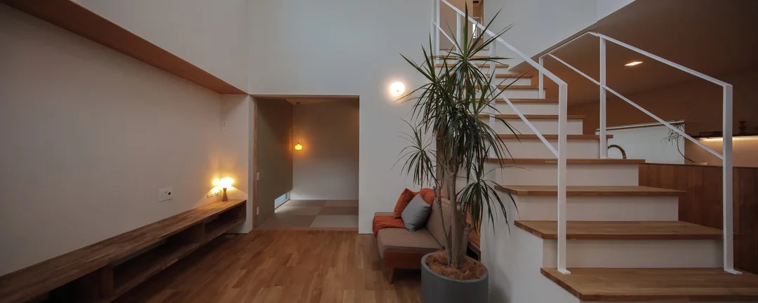 リビングの全景。吹き抜けの階段、木製のテレビボード、ソファがあり、奥には畳敷きの和室スペースが続いている