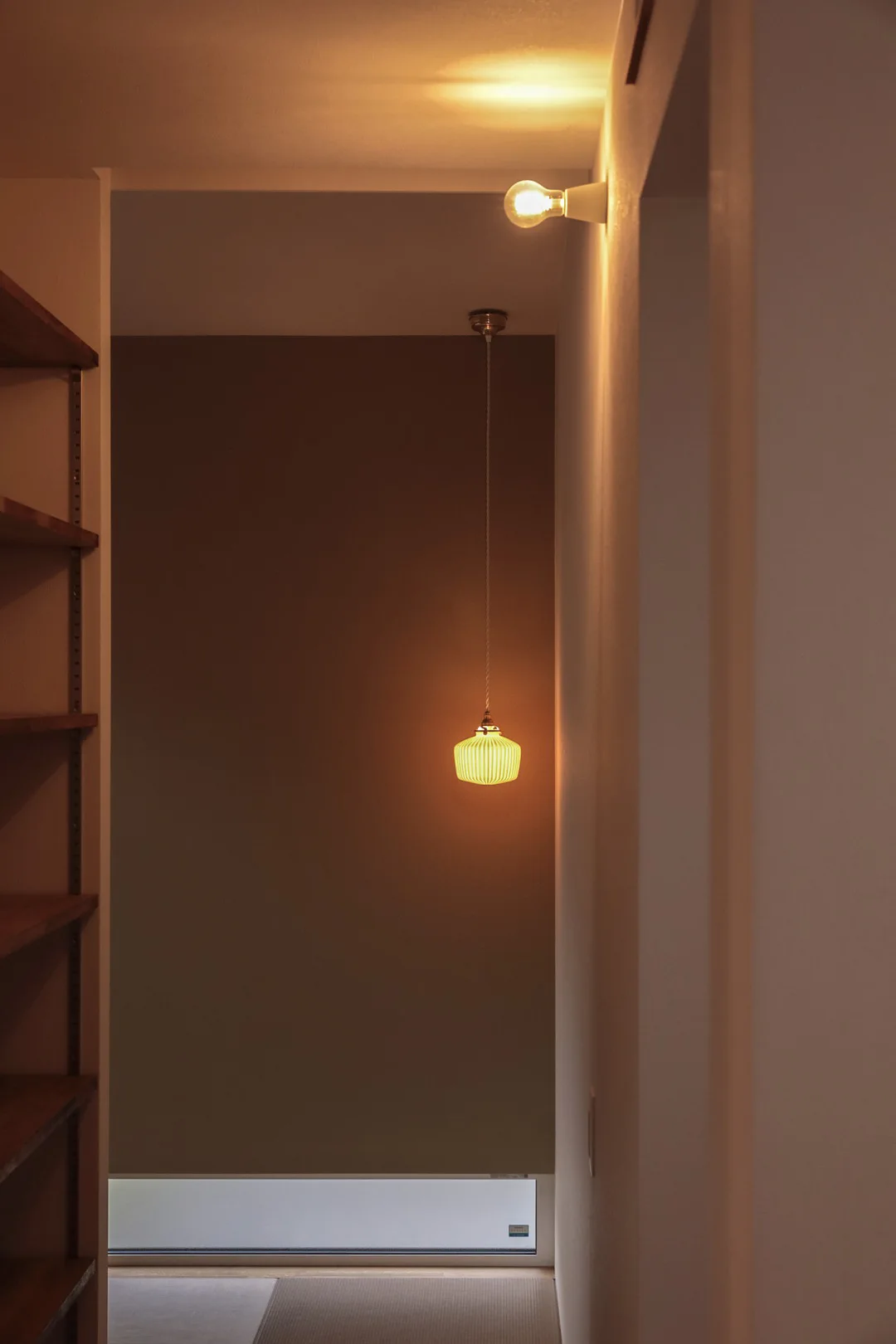 薄暗い畳スペースに吊るされた、レトロなデザインのガラスシェードを持つペンダントライトが温かい光を放っている