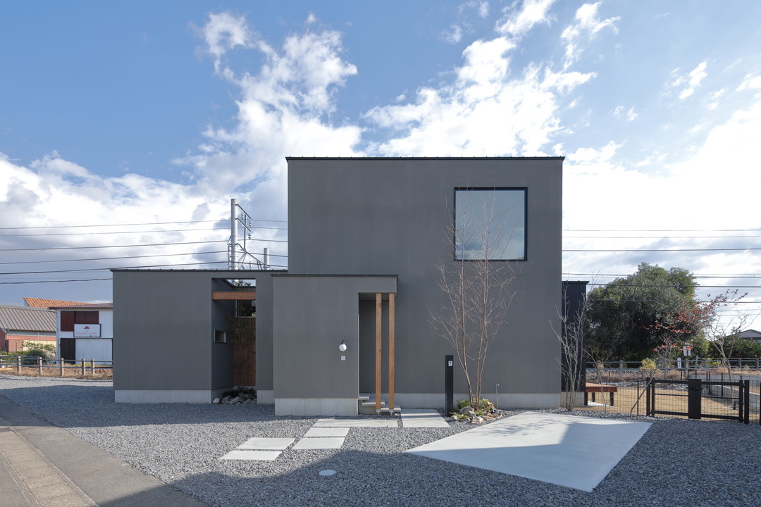 家の外観。青空、箱が2つ組み合わされたような見た目、グレーの壁の色