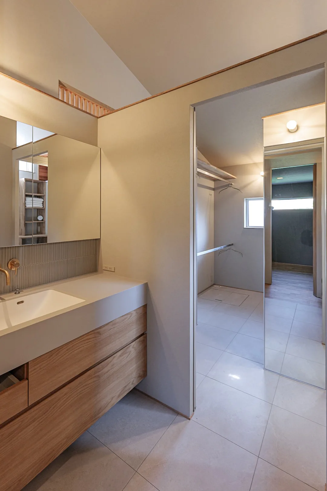 広いカウンターと鏡のある洗面台。奥には姿見のあるランドリールームと収納棚が見える。