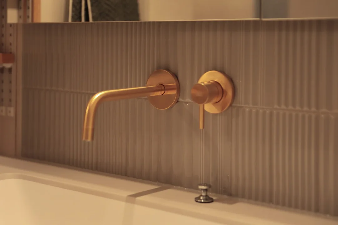 真鍮色（ゴールド）の壁出し水栓と、質感のあるグレーのバックタイルのアップ。