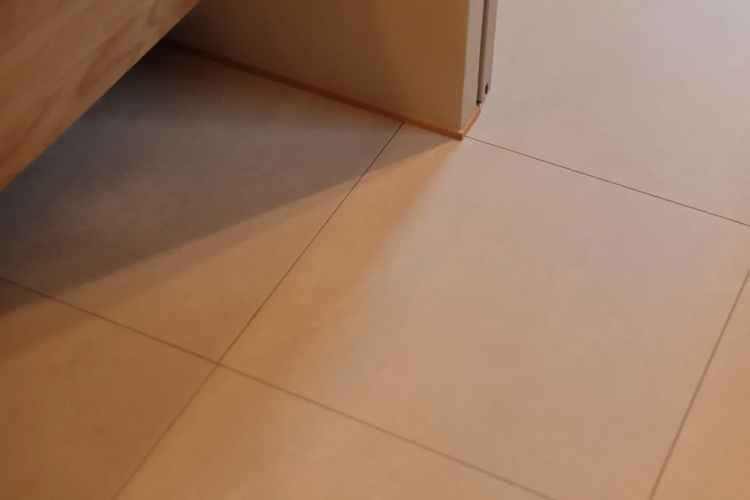 清潔感のあるベージュの大判タイル床に、照明の光が繊細な影をつくっている。