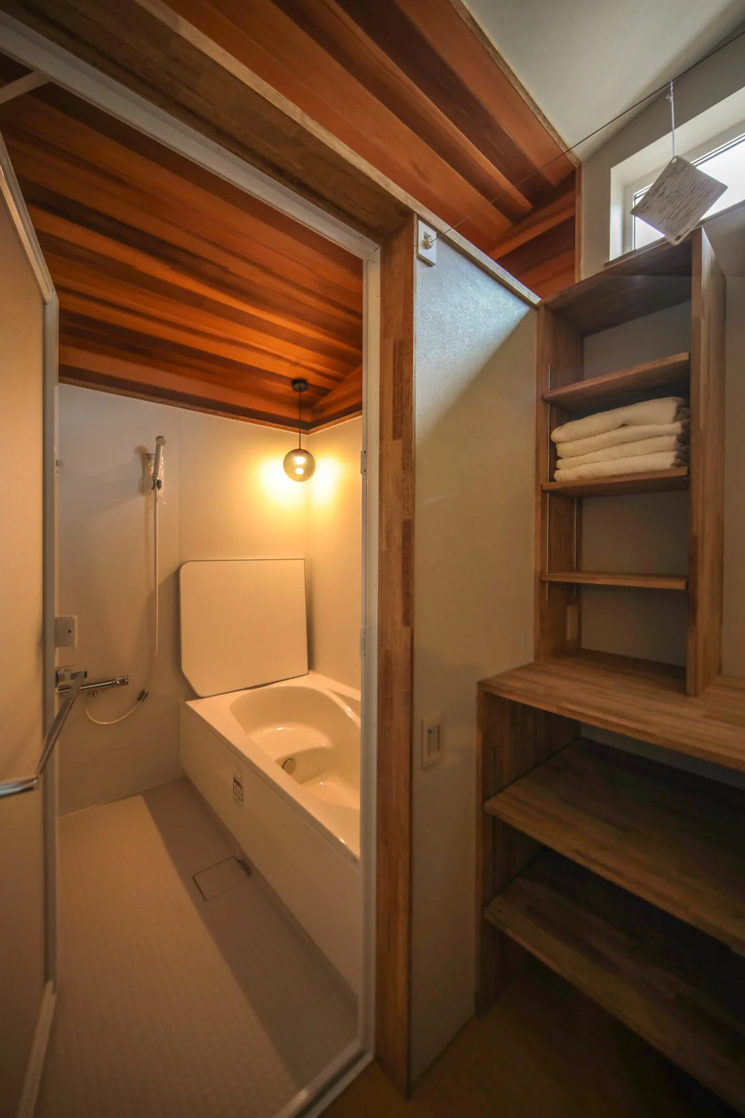 レッドシダーの羽目板が貼られた天井が特徴的なユニットバスと、隣接する脱衣室。造作のタオル収納棚がある。