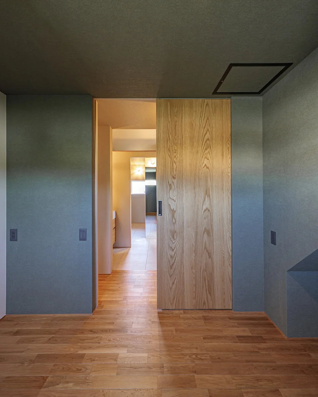 落ち着いたダークグリーンの壁面と、天井まであるダイナミックな木目の引き戸のついた主寝室。安眠できそうな暗さがある。