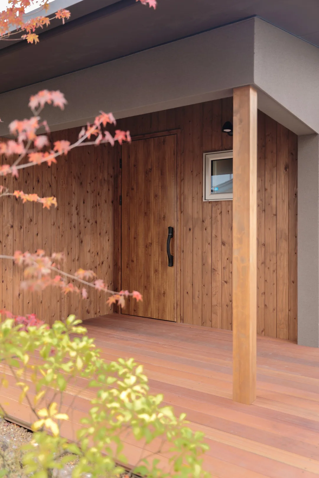 深い軒下のウッドデッキ製玄関ポーチと、温かみのある縦格の木目デザインが美しい玄関ドア。