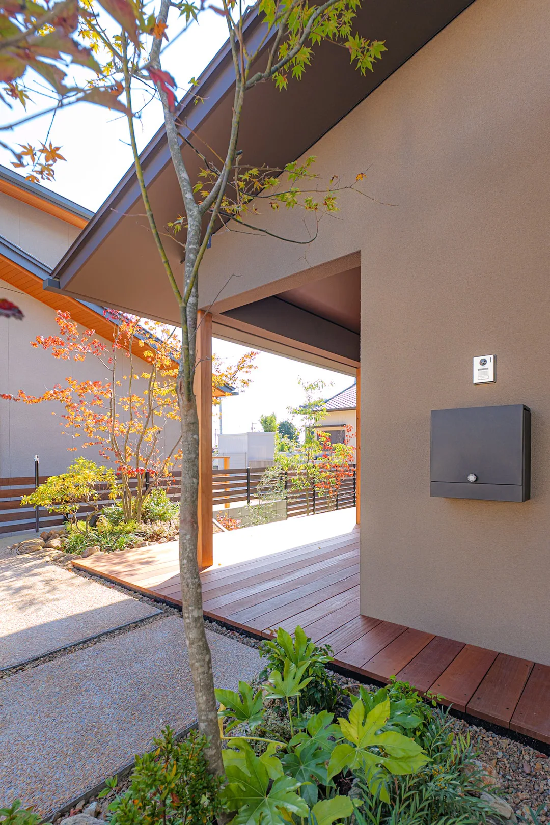 玄関ポーチのウッドデッキから庭を望む、開放感のある視線と木製支柱のディテール。