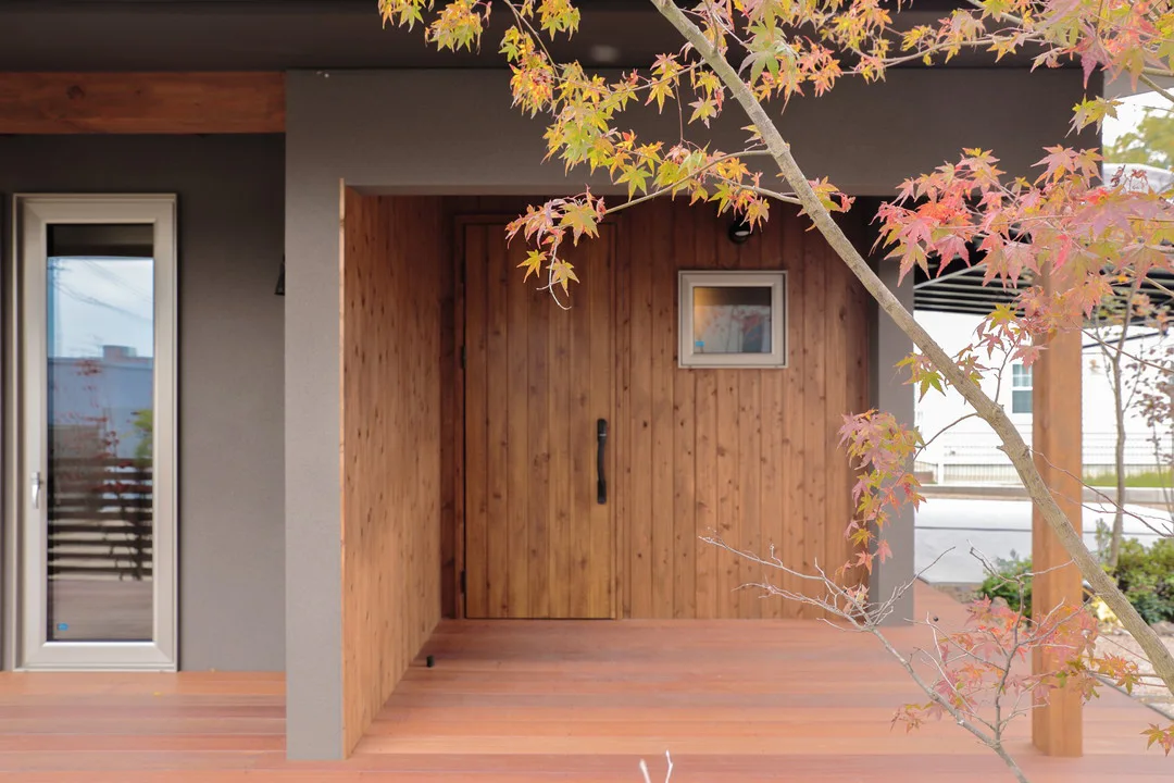 グレーの塗り壁と、天然木の壁、大きなガラスのテラスドアが調和したスタイリッシュな玄関周り。