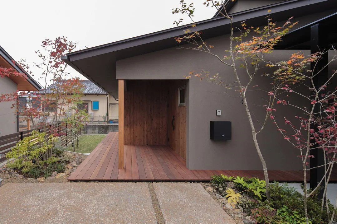 重厚感のあるグレーの外壁に設置されたシンプルな黒いポストと、足元の植栽。家の左右にはモミジなどの植栽がある。