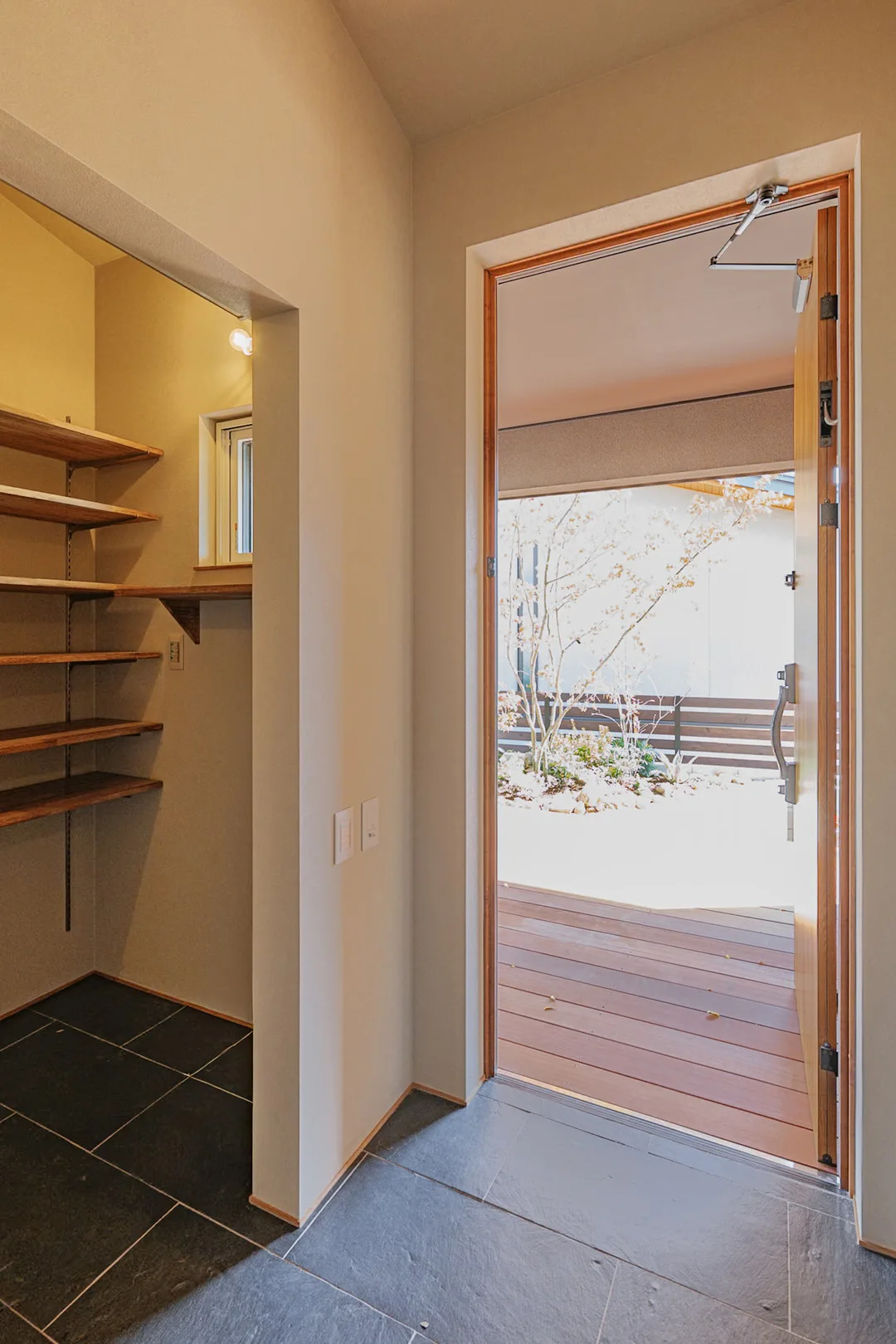 黒い玄昌石の土間から、開いたドア越しに庭の紅葉とウッドデッキを見る景色。