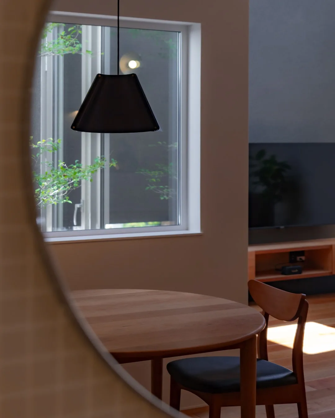 洗面室の鏡に映り込んだ、木製ダイニングテーブルと黒い照明、窓外の緑