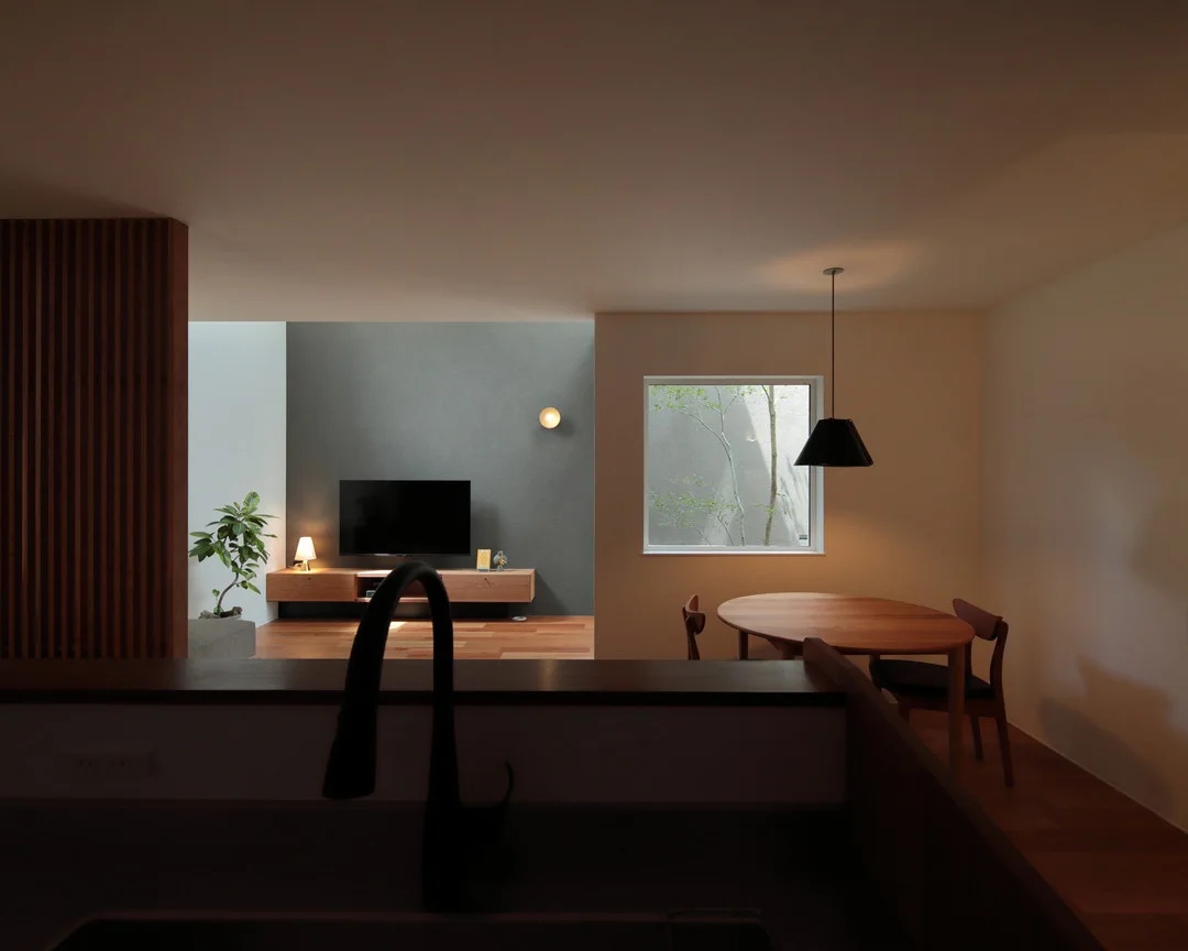 手前の水栓越しの視点。グレーのアクセントウォールがあるリビングと、中庭が見える正方形の窓